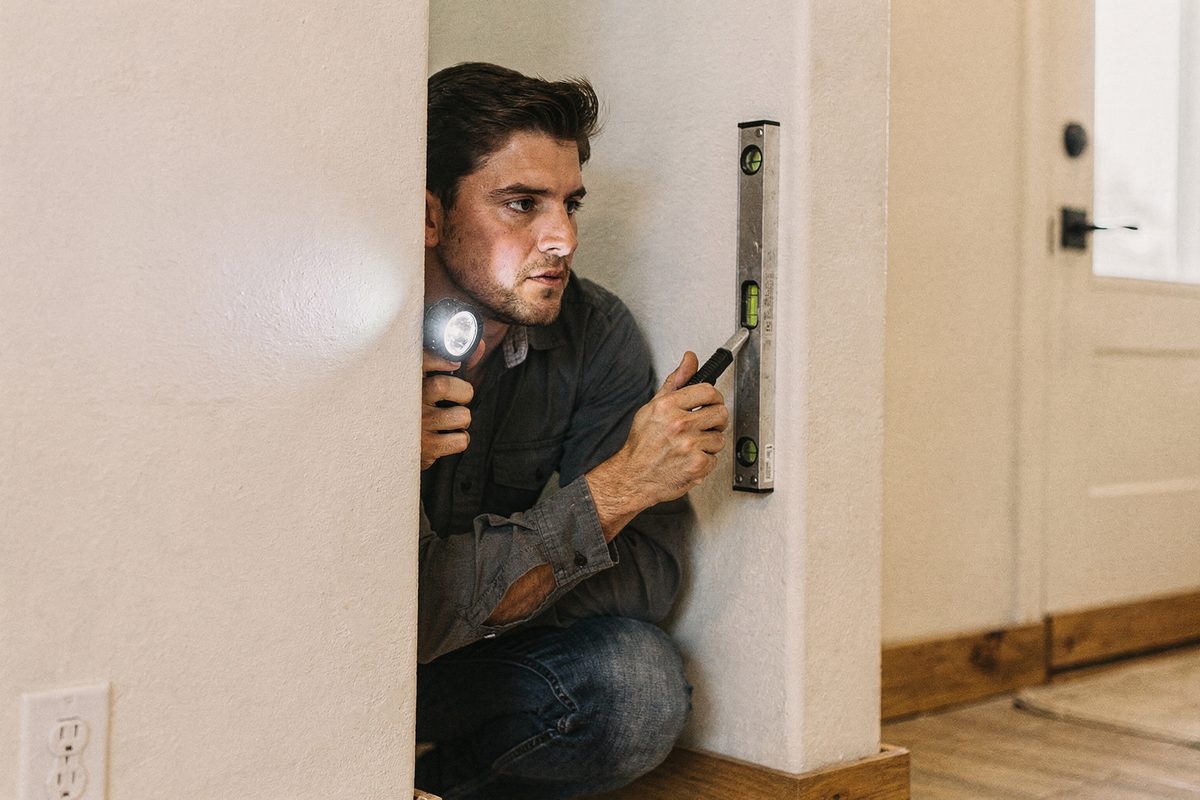 Worker checking a finished wall corner with a flashlight and a level